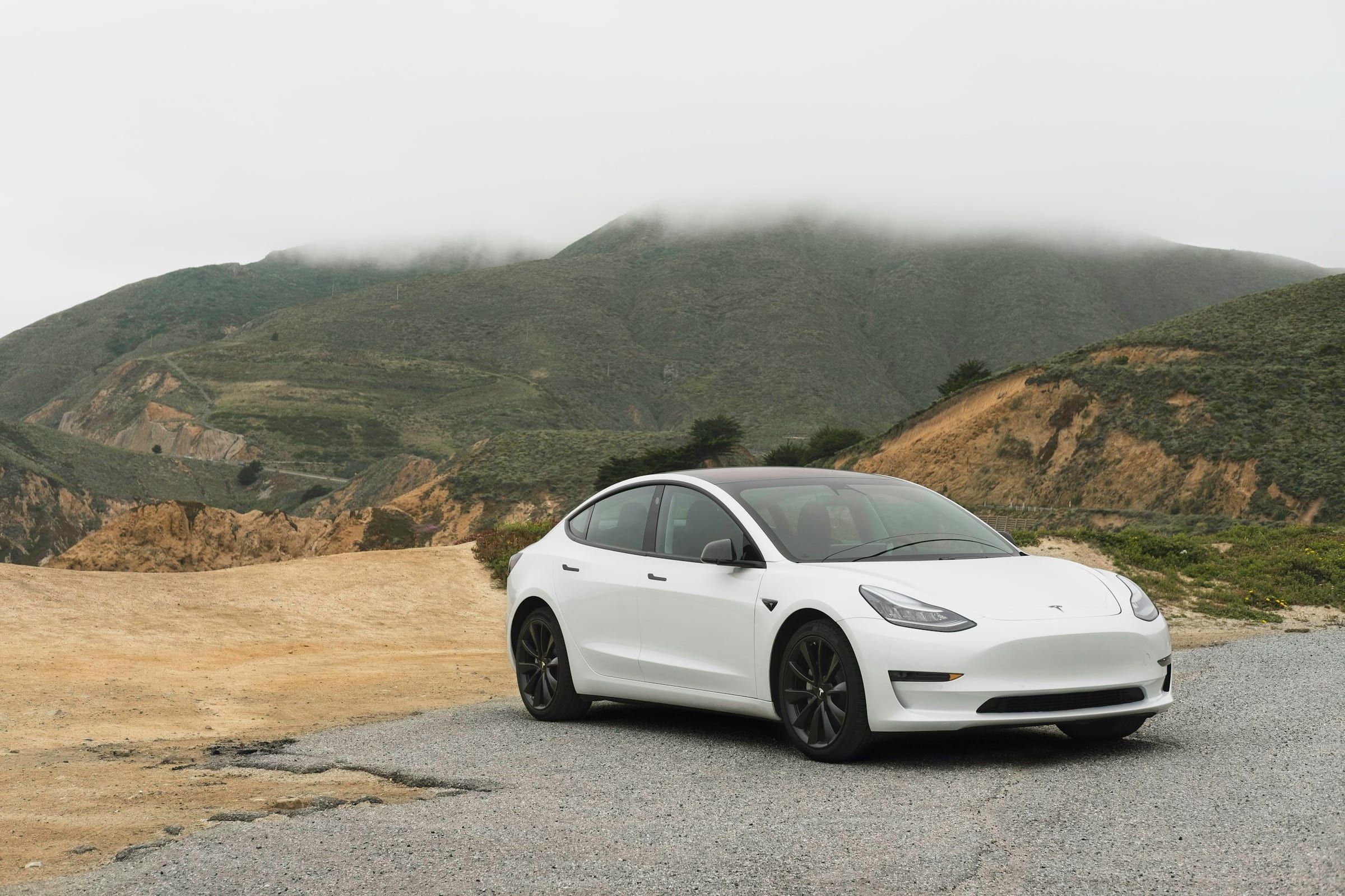 White Tesla Model 3 parked on a mountain road under an overcast sky