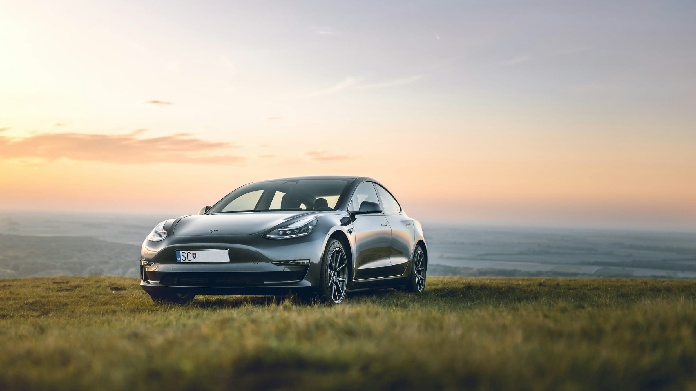 Dark Tesla Model 3 on a grass field at sunset