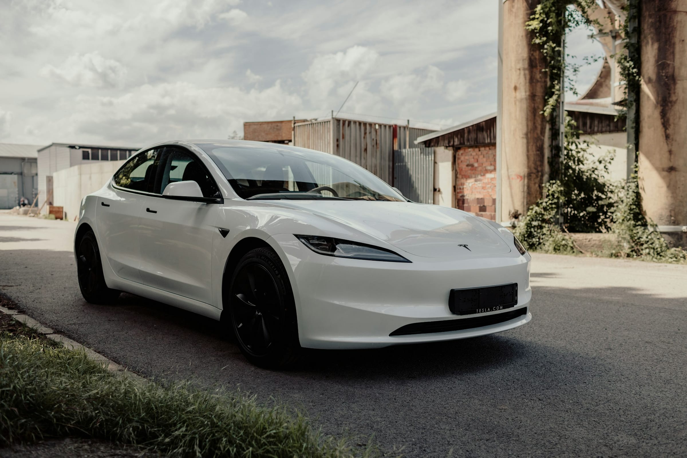 White Tesla Model 3 driving past an industrial building